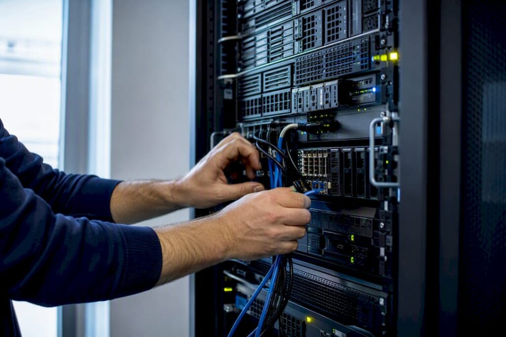 Hands plugging network cable into server rack